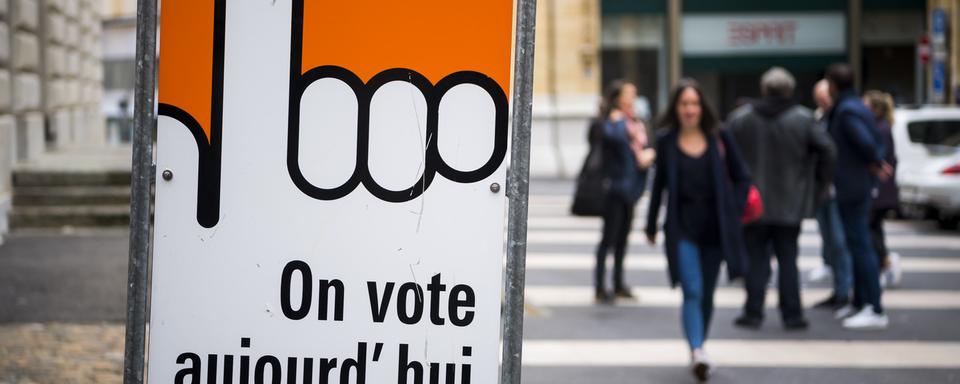 Des personnes marchent à côté d'un bureau de vote à Neuchâtel. Le canton a refusé le droit de vote à 16 ans en février 2020. [Keystone - Jean-Christophe Bott]