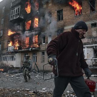 Un habitant quitte sa maison après que les bombardements russes ont détruit un immeuble d'habitation à Bakhmut, dans la région de Donetsk, en Ukraine, le 7 décembre 2022. [Keystone - AP Photo/LIBKOS]