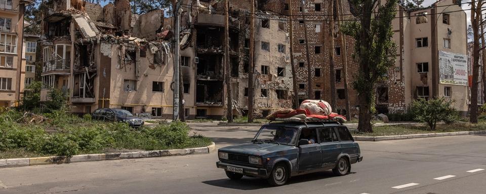 Une voiture roule à côté d'un bâtiment résidentiel endommagé à Irpin, près de Kiev, en Ukraine, le 16 juin 2022. [Keystone - ROMAN PILIPEY]