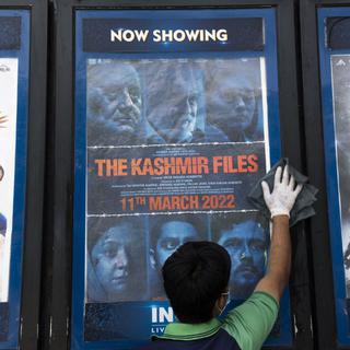 Un ouvrier nettoie un présentoir avec l’affiche du film The Kashmir Files devant un cinéma à New Delhi. [Xavier Galiana]