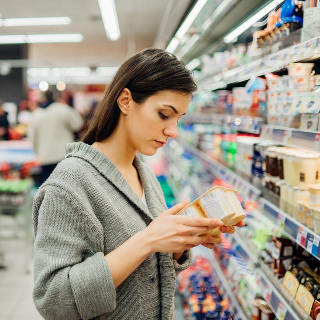 Une femme lit l'étiquette nutritionnelle sur des yaourts. [Depositphotos - eldarnurkovic]