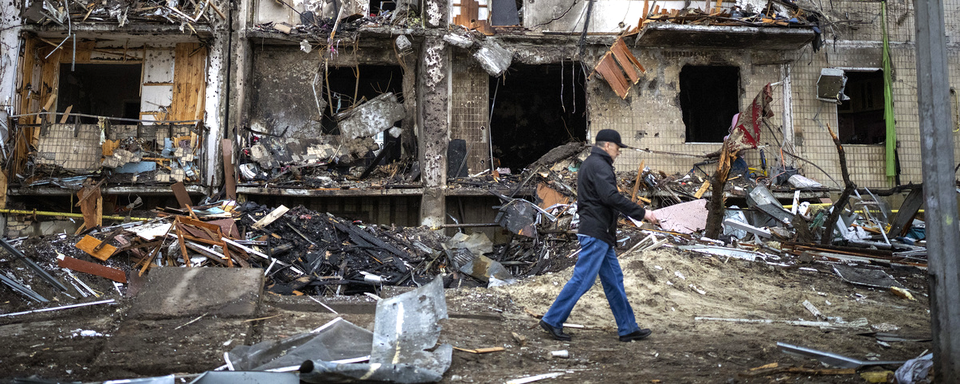 Un homme marchant devant un immeuble détruit à la suite d'un bombardement à Kiev. [AP Photo/Keystone - Emilio Morenatti]