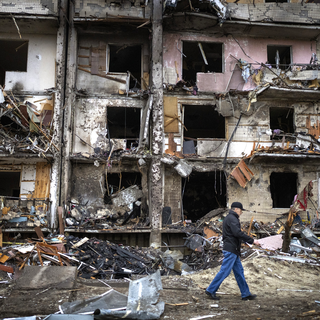Un homme marchant devant un immeuble détruit à la suite d'un bombardement à Kiev. [AP Photo/Keystone - Emilio Morenatti]
