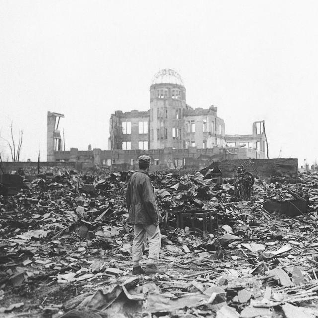 Sur cette photo d'archive de 1945, un correspondant de guerre allié se tient dans les ruines d'Hiroshima, au Japon, quelques semaines après que la ville a été rasée par une bombe atomique. [AP Photo/File/KEYSTONE]
