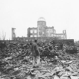 Sur cette photo d'archive de 1945, un correspondant de guerre allié se tient dans les ruines d'Hiroshima, au Japon, quelques semaines après que la ville a été rasée par une bombe atomique. [AP Photo/File/KEYSTONE]