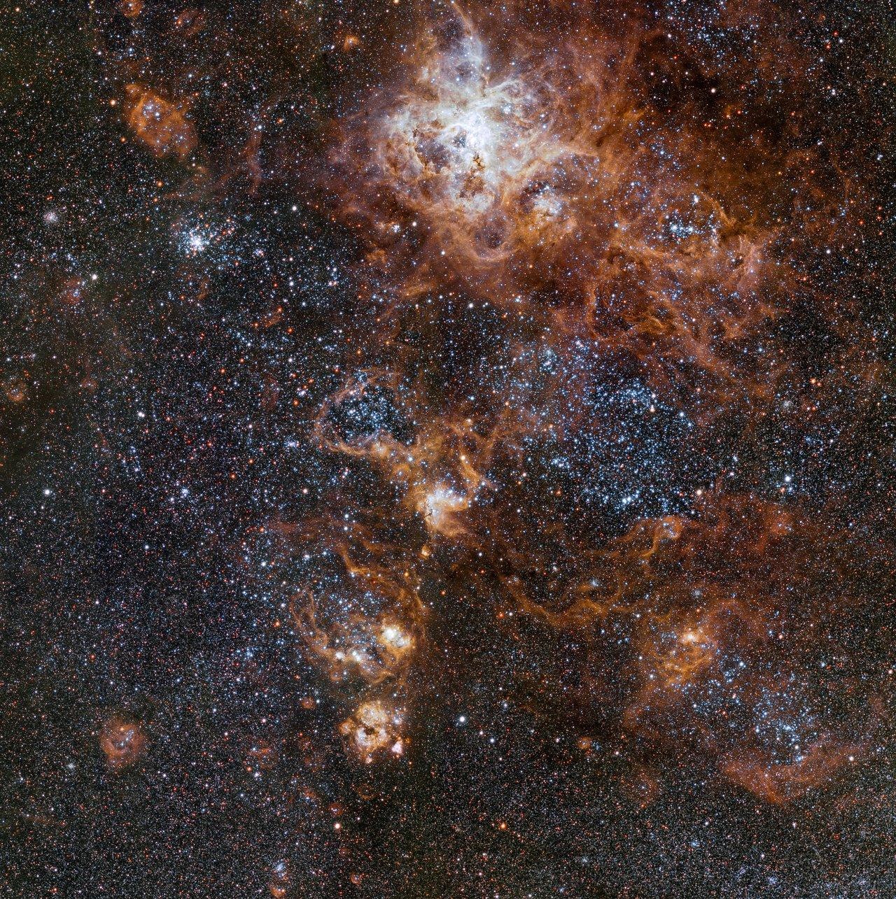 A quelque 160'000 années lumière brille la Nébuleuse de la Tarentule, la structure la plus spectaculaire du Grand Nuage de Magellan. Cette région révèle un paysage céleste constellé d'amas stellaires, de nuages de gaz brillant ainsi que de restes épars d'explosions de supernovae. [ESO]