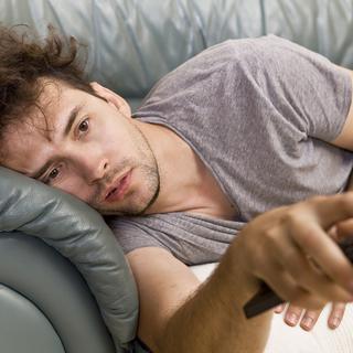 Une personne allongée sur son canapé avec une télécommande dans la main. (image d'illustration) [Depositphotos - lukas_zb]