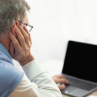 Une personne âgée de dos, face à son ordinateur. [Depositphotos - Milkos]