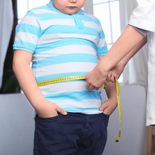 Un enfant en surpoids se fait mesurer son tour de taille par un médecin. [Depositphotos - belchonock]