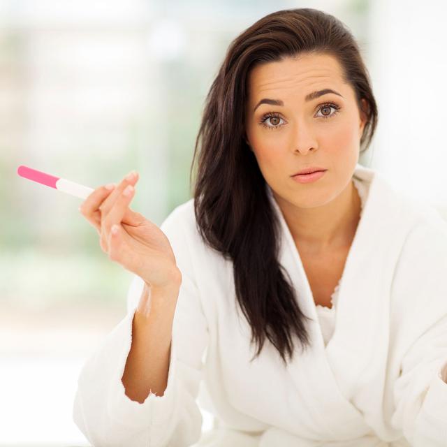 Une femme tient un test de grossesse avec un air interrogateur. [Depositphotos - michaeljung]