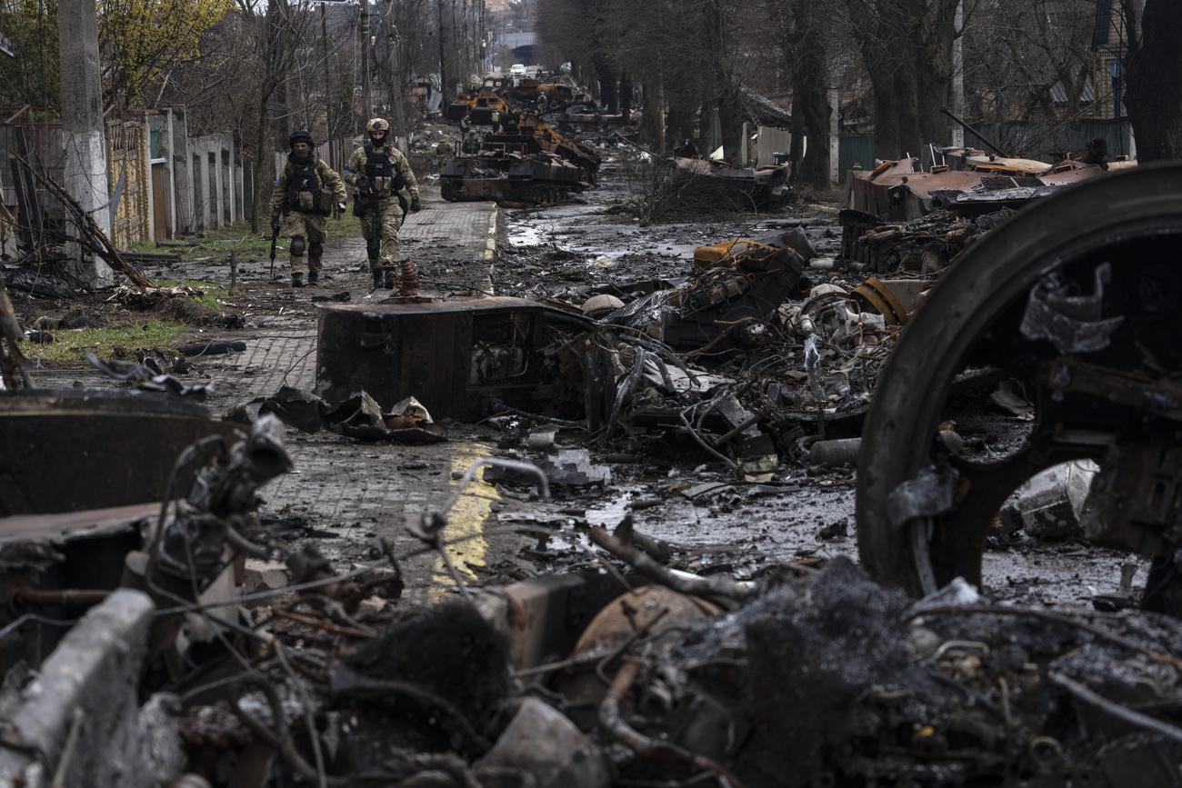 Des soldats ukrainiens marchent le long d'une colonne de chars russes détruits à Boutcha. [Keystone/AP Photo - Rodrigo Abd]