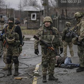 Des soldats ukrainiens près du cadavre d'un homme habillé en civil dans la localité de Boutcha, occupée précédemment par les Russes. [Keystone/AP Photo - Vadim Ghirda]