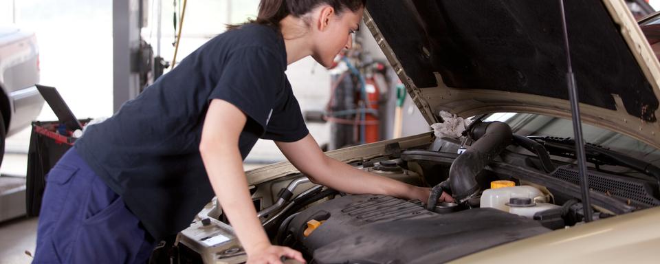 Une garagiste examine un moteur de voiture. [Depositphotos - SimpleFoto]