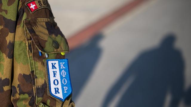 Un écusson "Kfor" sur la tenue d'un militaire suisse du contingent de la Swisscoy marchant dans la partie suisse du Camp Marechal de Lattre de Tassigny-Camp Novo, au Kossovo. [Keystone - Jean-Christophe Bott]