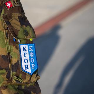 Un écusson "Kfor" sur la tenue d'un militaire suisse du contingent de la Swisscoy marchant dans la partie suisse du Camp Marechal de Lattre de Tassigny-Camp Novo, au Kossovo. [Keystone - Jean-Christophe Bott]