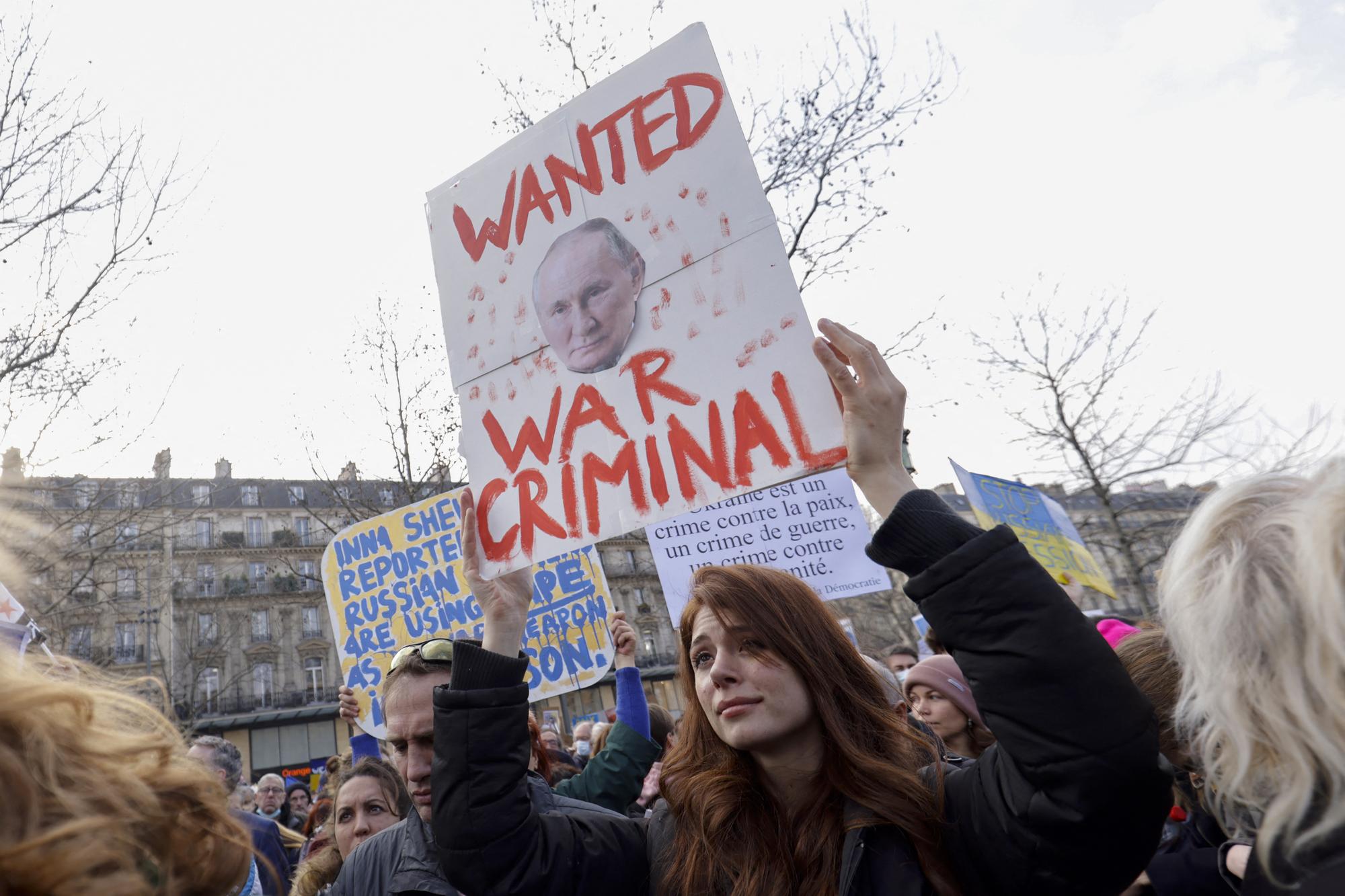Une manifestante tient une banderole avec le visage de Vladimir Poutine lors d'une manifestation contre l'invasion militaire de l'Ukraine par la Russie, sur la Place de la République à Paris. [AFP - Sameer Al-Doumy]