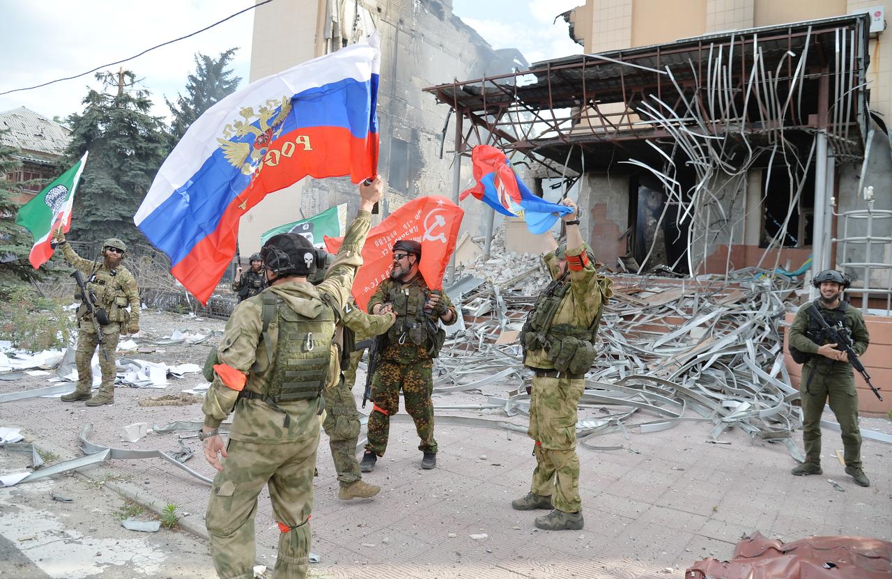 Des forces russes et des membre du régiment Kadirov tchétchène agitent leurs drapeaux devant le bâtiment de l'administration municipale de Lyssytchansk, le 2 juillet 2022. [Sputnik/AFP - Viktor Antonyuk]