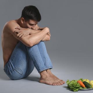 Un jeune homme anorexique regarde avec anxiété des fruits et légumes. [Depositphotos - Serezniy]
