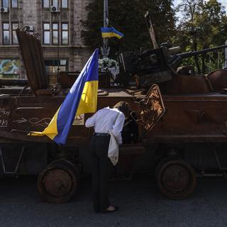 Une femme avec un drapeau ukrainien observe un tank russe détruit à Kiev, Ukraine. [Keystone/AP Photo - David Goldman]