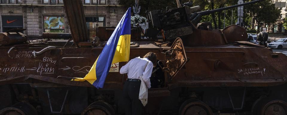 Une femme avec un drapeau ukrainien observe un tank russe détruit à Kiev, Ukraine. [Keystone/AP Photo - David Goldman]