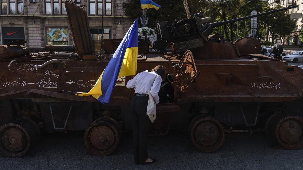 Une femme avec un drapeau ukrainien observe un tank russe détruit à Kiev, Ukraine. [Keystone/AP Photo - David Goldman]
