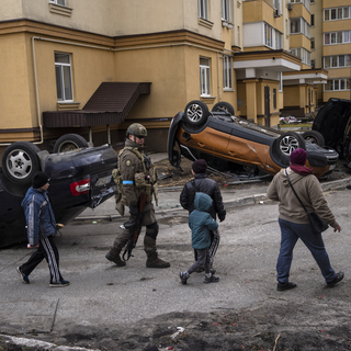 Un soldat ukrainien marche avec des enfants devant des voitures détruites à cause de la guerre contre la Russie, à Bucha, dans la banlieue de Kiev, en Ukraine, lundi 4 avril 2022.