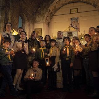 Des membres de l’organisation scoute ukrainienne "Plast" tiennent des lumières de la paix lors d’un service religieux de Noël à Kharkiv. [AP Photo/Keystone - Evgeniy Maloletka]