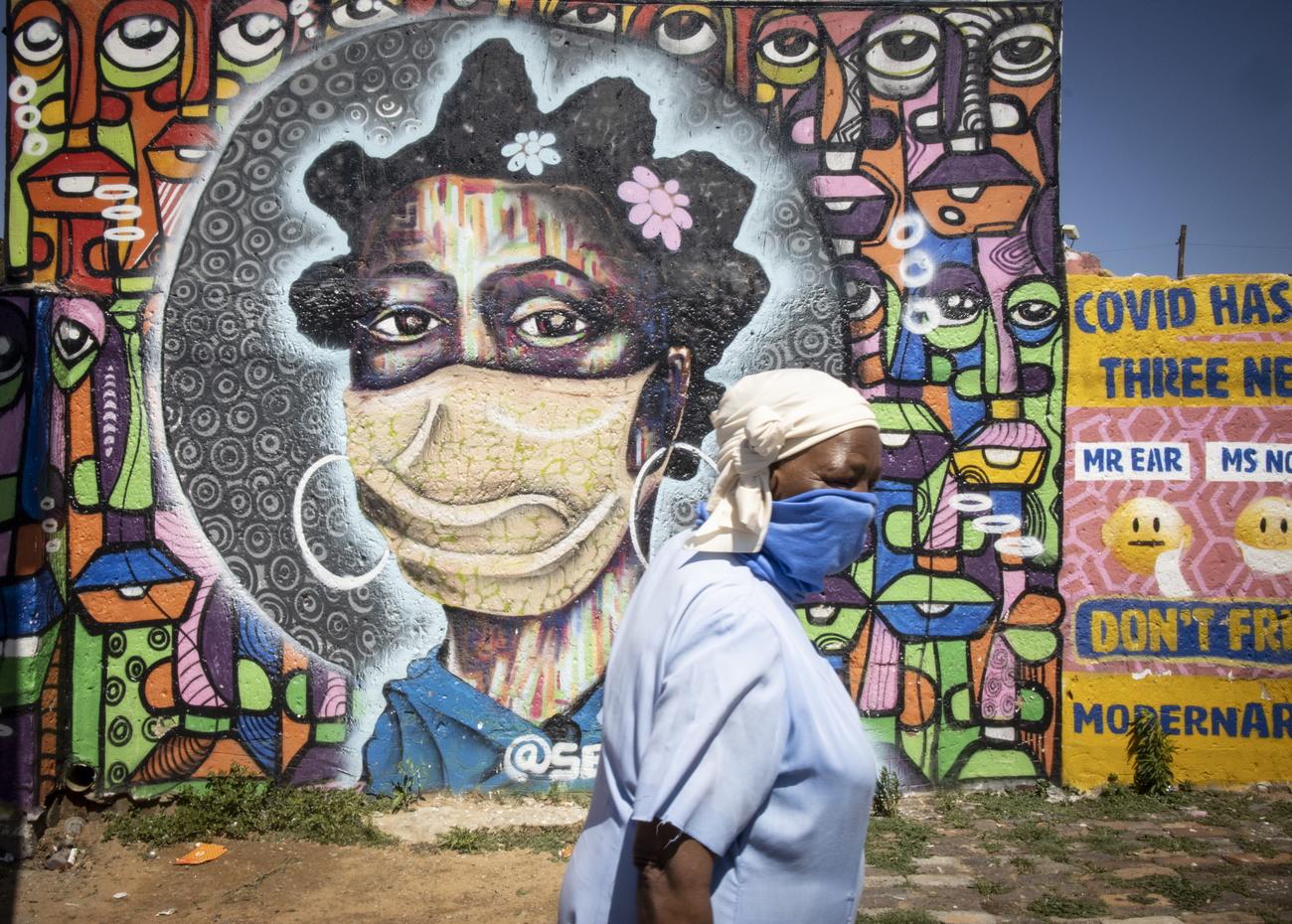 Une femme masquée devant une fresque à Soweto, en Afrique du Sud. [EPA/Keystone - Kim Ludbrook]