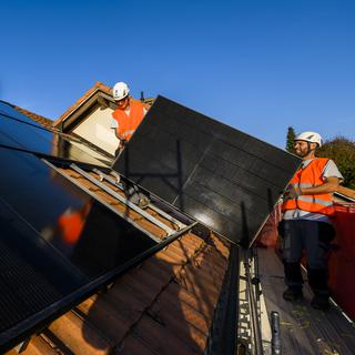 Deux installateurs du Groupe E installent un panneau solaire photovoltaique sur le toit d'une habitation le mercredi 2 novembre 2022 à Fribourg. [Keystone - Jean-Christophe Bott]