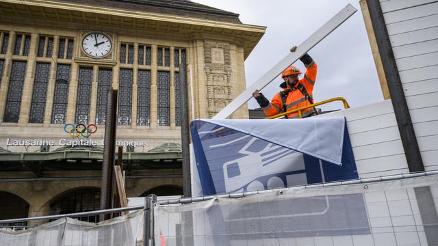 Un ouvrier démonte la palissade de chantier devant la gare de Lausanne. [Keystone - Jean-Christophe Bott]