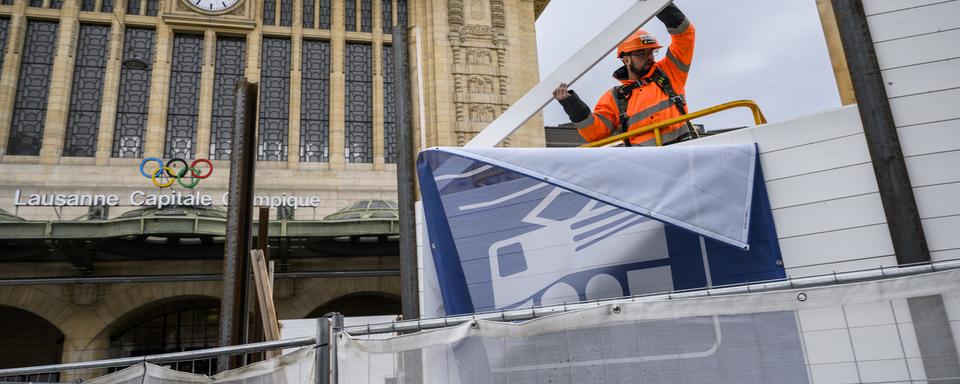 Un ouvrier démonte la palissade de chantier devant la gare de Lausanne. [Keystone - Jean-Christophe Bott]