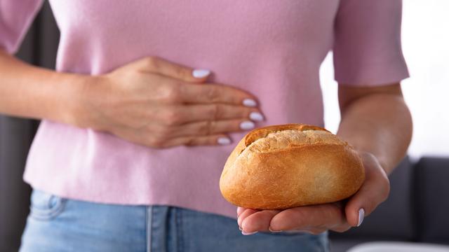 Une femme se tient de ventre en regardant un pain qu'elle tient dans sa main. [Depositphotos - AndreyPopov]