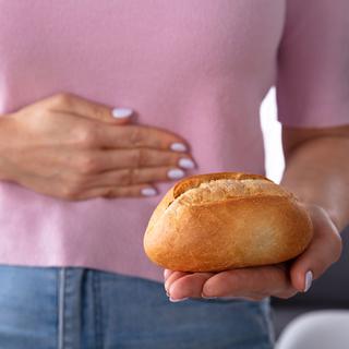 Une femme se tient de ventre en regardant un pain qu'elle tient dans sa main. [Depositphotos - AndreyPopov]
