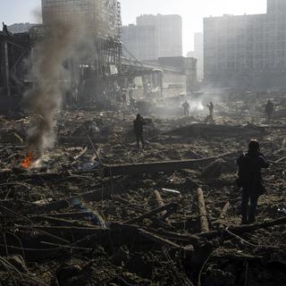 Des personnes se rassemblent au milieu des destructions causées par le bombardement d'un centre commercial, à Kiev, en Ukraine, le lundi 21 mars 2022. [AP Photo/KEYSTONE - Rodrigo Abd]