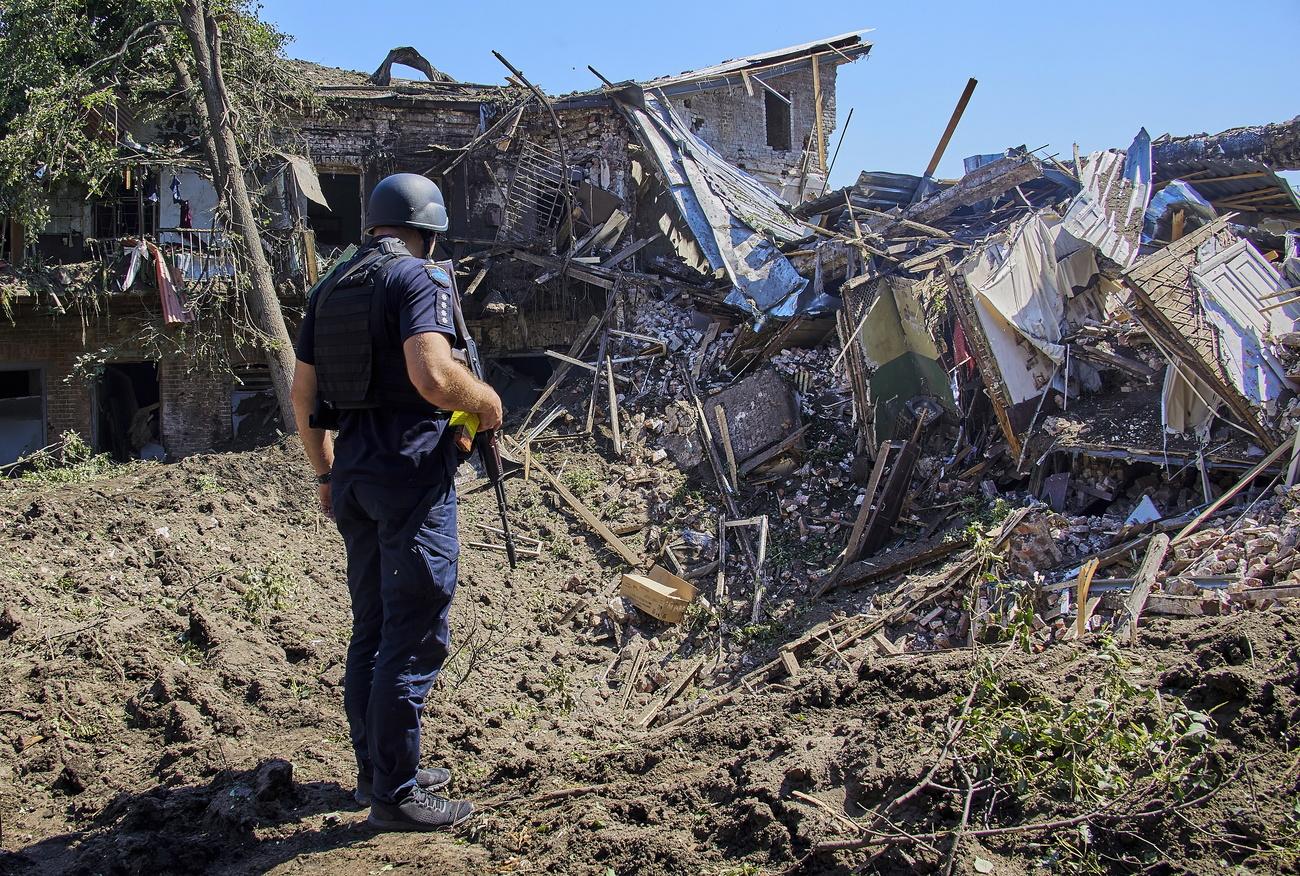 Un policier inspecte les ruines d'un bâtiment détruit par un bombardement près de Kharkiv, dans l'est de l'Ukraine, le 9 juillet 2022. [Keystone - EPA/SERGEY KOZLOV]