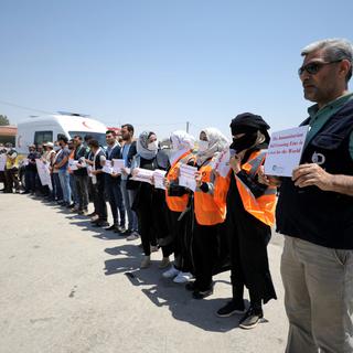 Des militants et des travailleurs de la société civile et des organisations d'aide humanitaire et médicale tiennent des pancartes lors d'un rassemblement appelant la communauté internationale à maintenir le corridor humanitaire transfrontalier, au poste frontière de Bab Al-Hawa, à Idlib, en Syrie, le 7 juillet 2022. [EPA/Keystone - Yahya Nemah]