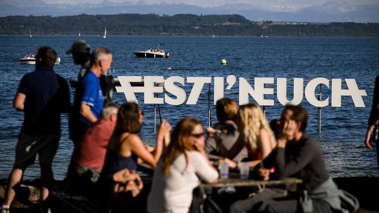 Des personnes profitent de l'ambiance au bord du lac devant le logo du festival Festi'Neuch, le vendredi 10 juin 2022 à Neuchâtel. [KEYSTONE - Jean-Christophe Bott]
