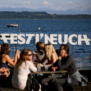 Des personnes profitent de l'ambiance au bord du lac devant le logo du festival Festi'Neuch, le vendredi 10 juin 2022 à Neuchâtel. [KEYSTONE - Jean-Christophe Bott]