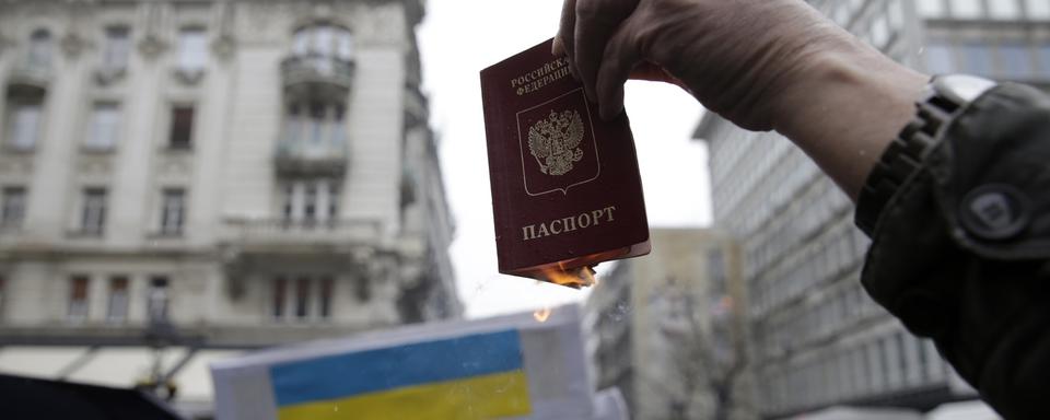 Une homme brûle son passeport russe lors d'une manifestation contre la guerre en Ukraine à Belgrade, en Serbie. [Keystone - EPA/Andrej Cukic]