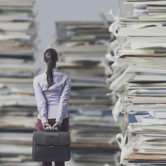 Une personne se tient devant des piles géantes de paperasse. [Depositphotos - stokkete]