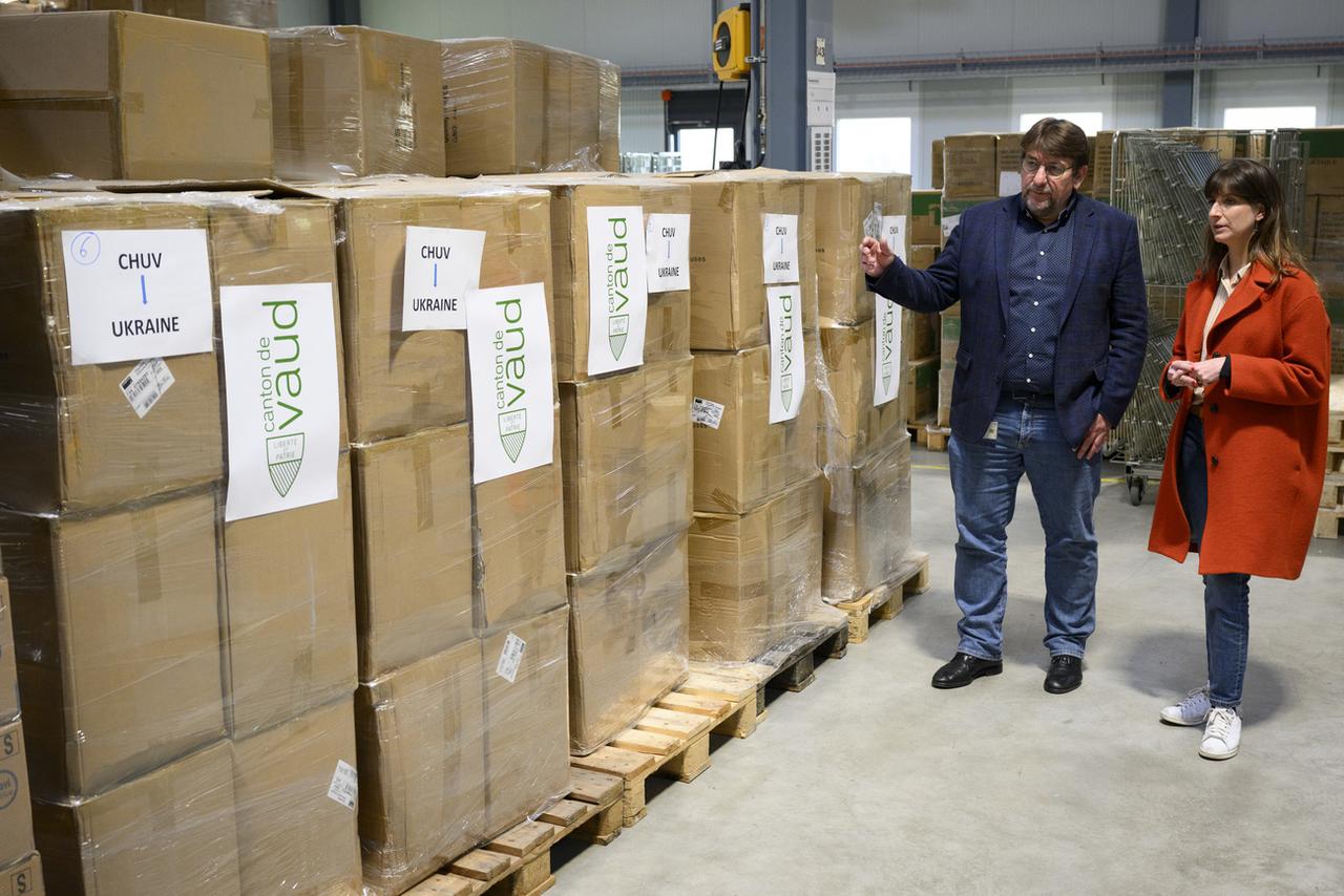 Pierre-Yves Müller, directeur de la logistique du CHUV, avec la conseillère d'Etat vaudoise Rebecca Ruiz, devant les palettes de matériel sanitaire. [Keystone - Laurent Gillieron]