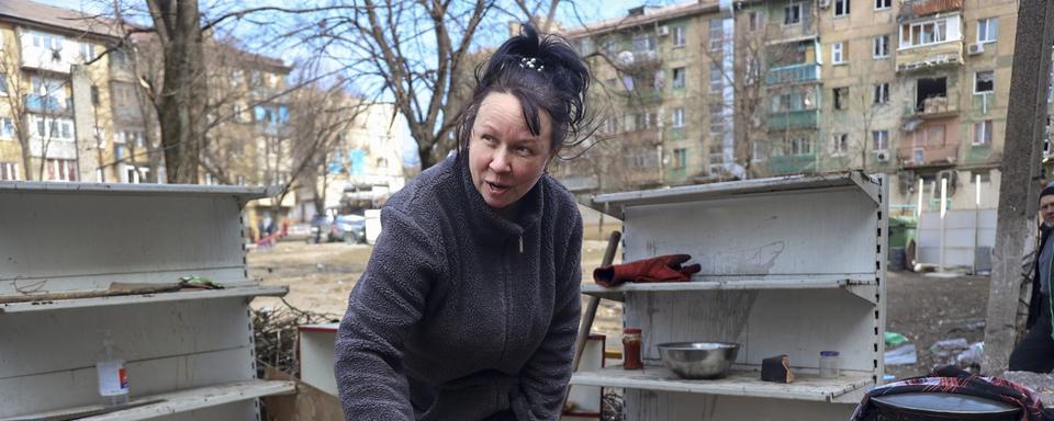 Une femme cuisine dans une cour d'immeubles d'habitation endommagés par les bombardements des combats à la périphérie de Mariupol, en Ukraine, dans le territoire contrôlé par le gouvernement séparatiste de la République populaire de Donetsk, le mardi 29 mars 2022. [AP Photo/KEYSTONE - Alexei Alexandrov]