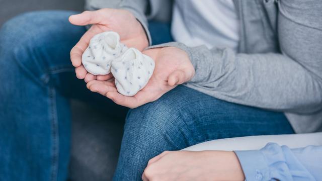 Gros plan sur les mains d'un couple qui tiennent des chaussons de nourrisson. [Depositphotos - AndrewLozovyi]