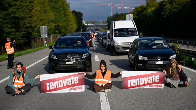 Des militants écologistes membres de Renovate Switzerland se sont assis sur la route lors d'une action de blocage de l'autoroute A1 à l'entrée de Lausanne, mardi 4 octobre 2022. [KEYSTONE - Laurent Gillieron]