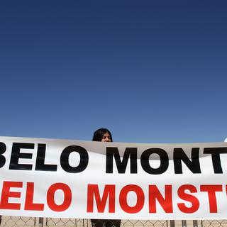 Des Indiens de l'ethnie Tucano de l'État du Para, dans le nord du Brésil, protestent contre la construction du barrage de Belo Monte devant le palais présidentiel à Brasilia, au Brésil, alors qu'une cérémonie de signature du contrat de construction du barrage se déroule à l'intérieur du palais, jeudi 26 août 2010. La pancarte indique en portugais : "Belo Monte : beau monstre". [AP Photo/KEYSTONE - Eraldo Peres]