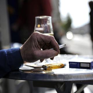 Un homme fumant une cigarette sur une terrasse. [Keystone - Dominic Favre]