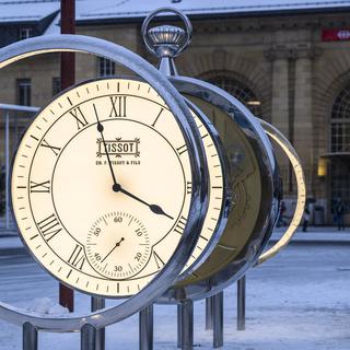 Une personne regarde la nouvelle horloge sur la place de la Gare à La Chaux-de-Fonds. [Keystone - Jean-Christophe Bott]