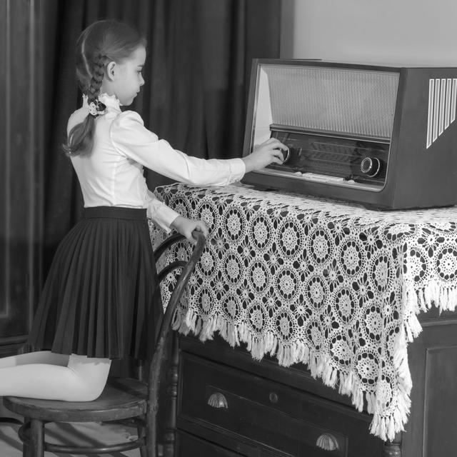 Une petite fille règle le volume d'une vieille radio. [Depositphotos - lotosfoto1]