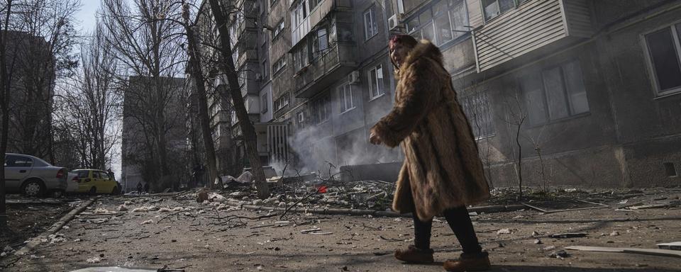 Une femme se déplace dans une rue de Marioupol, en Ukraine, après un bombardement russe le 13 mars 2022. [Keystone - AP Photo/Evgeniy Maloletk]