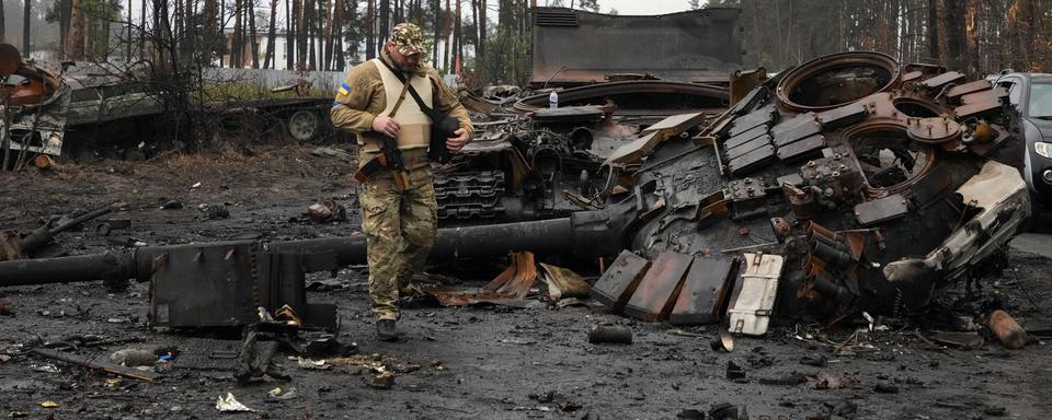 Soldat ukrainien devant un char russe détruit à Dmytrivka, près de Kiev, 02.04.2022. [AP/Keystone - Efrem Lukatsky]